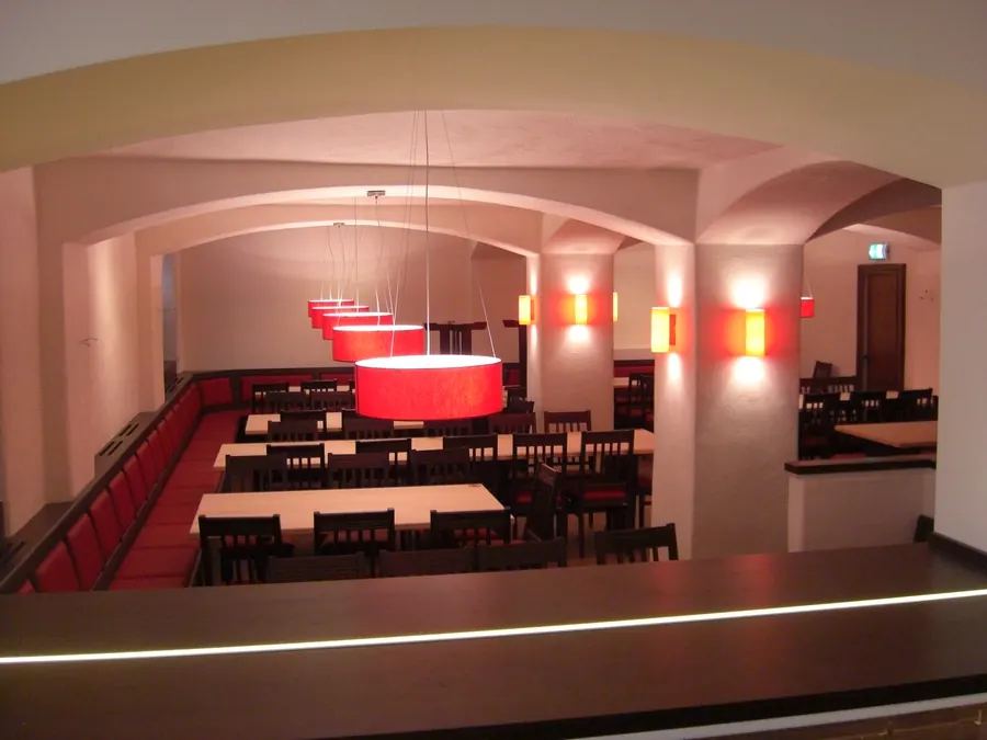 Gewölbesaal mit warm beleuchteter Bar und farbigen Wandleuchten