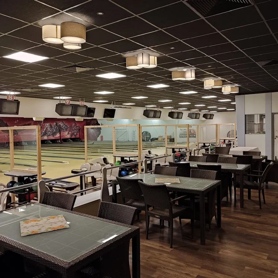 Bowlingbahnen mit Deckenleuchten und Sitzgruppen im Gastrobereich davor